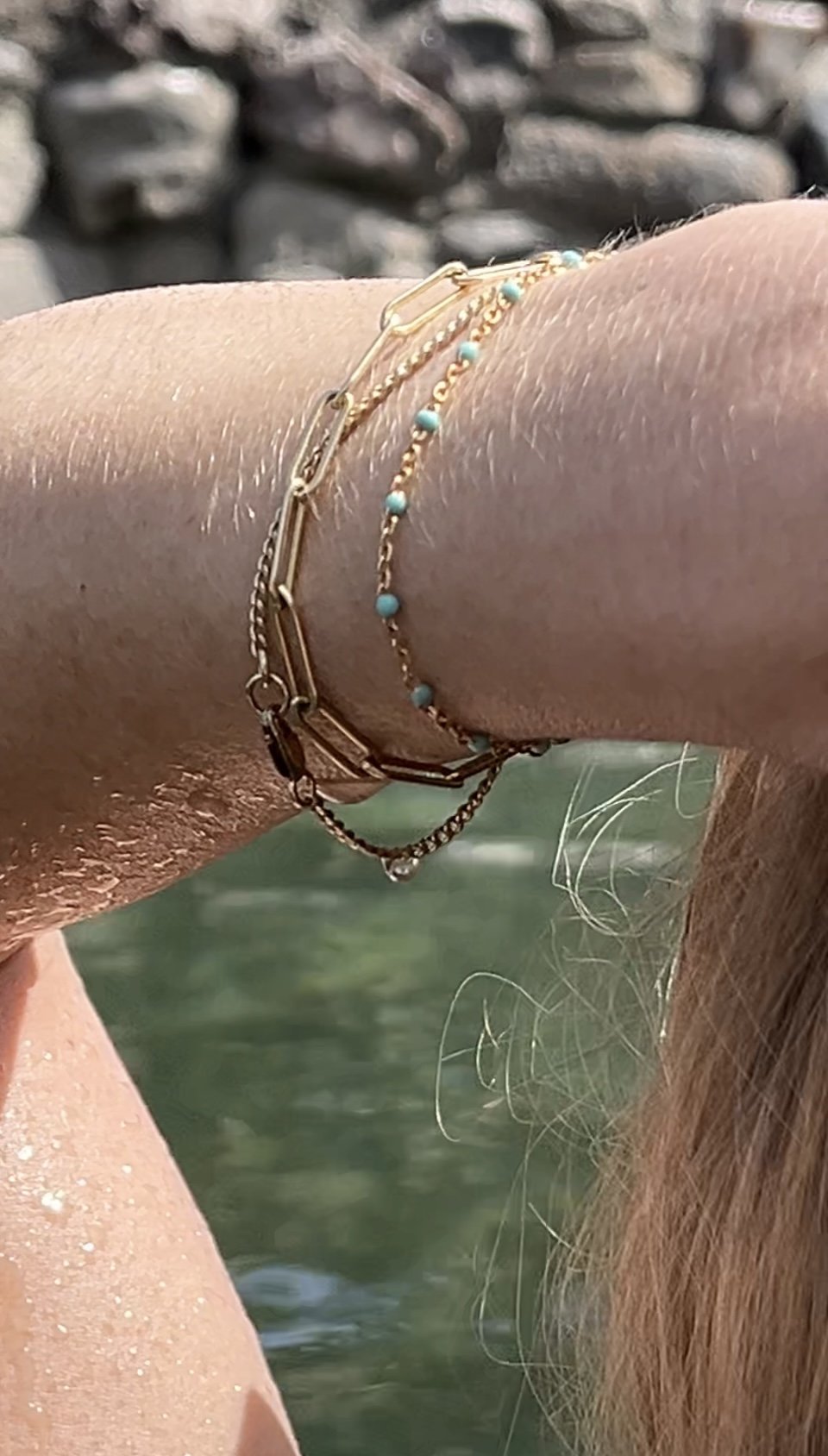 Detailed close-up of bracelets on model’s wrist in hot springs, highlighting the turquoise enamel bead bracelet in gold-filled