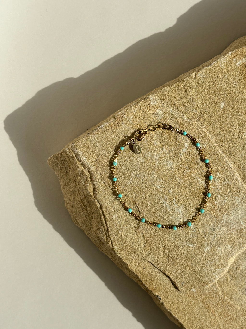 Product shot of turquoise enamel bead bracelet in yellow gold-filled, styled on a rock, bird’s-eye view