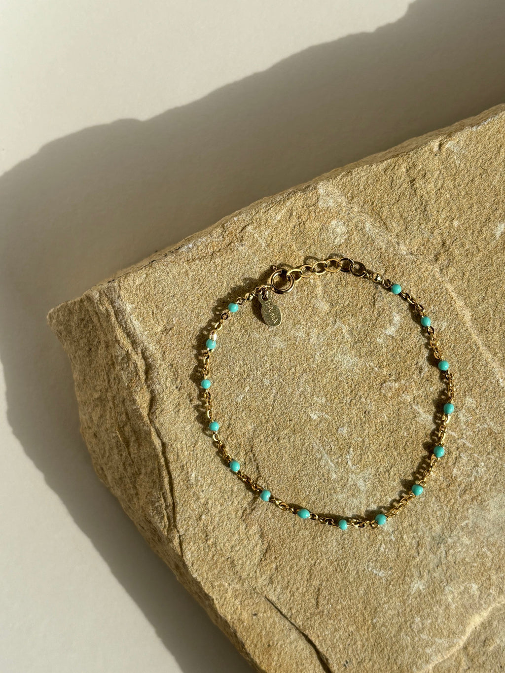 Closer bird’s-eye view of turquoise enamel bead bracelet on rock with natural backdrop