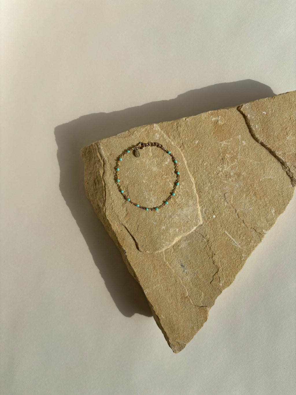 Wide bird’s-eye view of turquoise enamel bead bracelet in yellow gold-filled on rock, styled as product shot