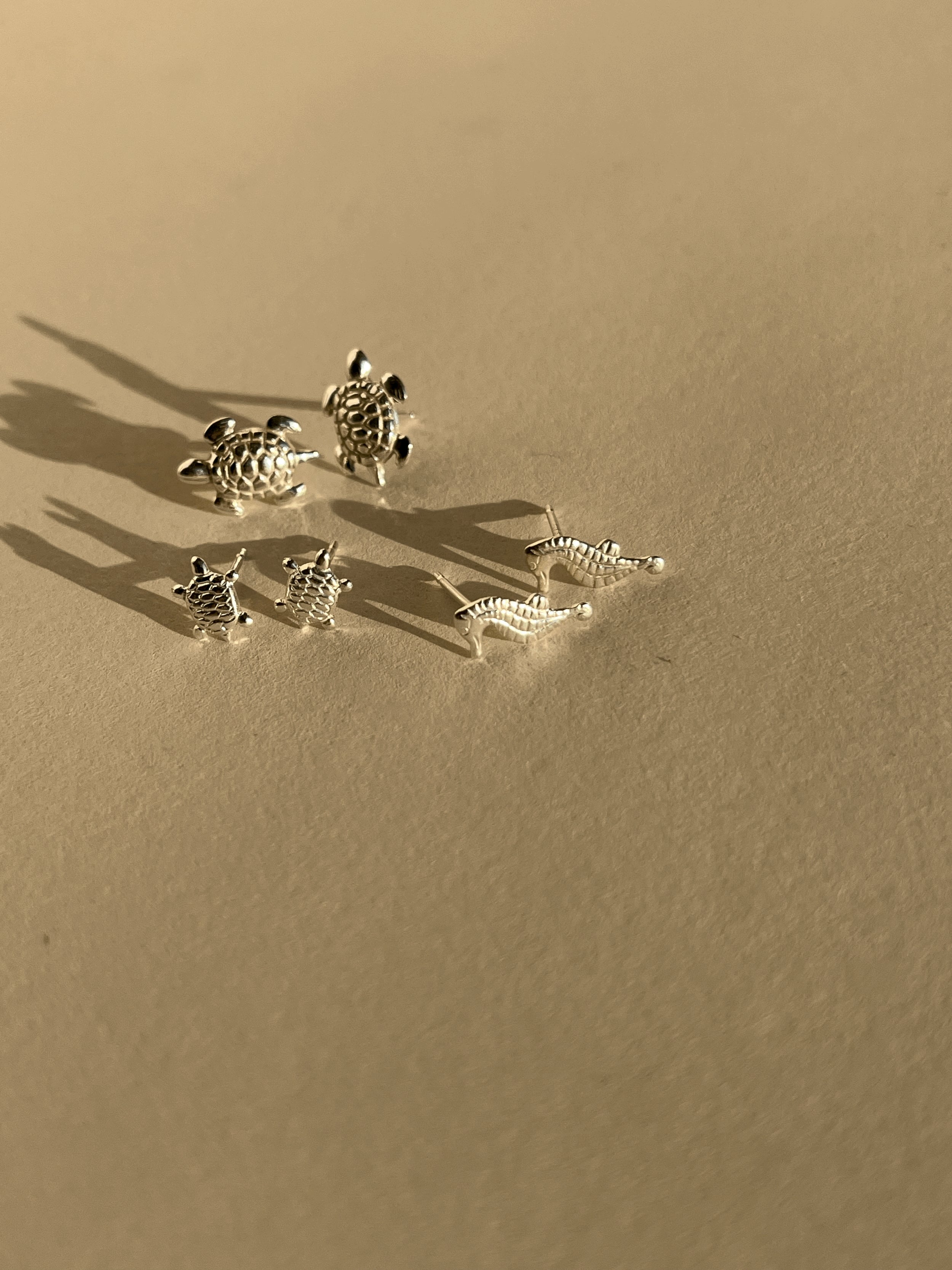 Close-up of pairs of large turtle, small turtle, and seahorse sterling silver stud earrings on a neutral background