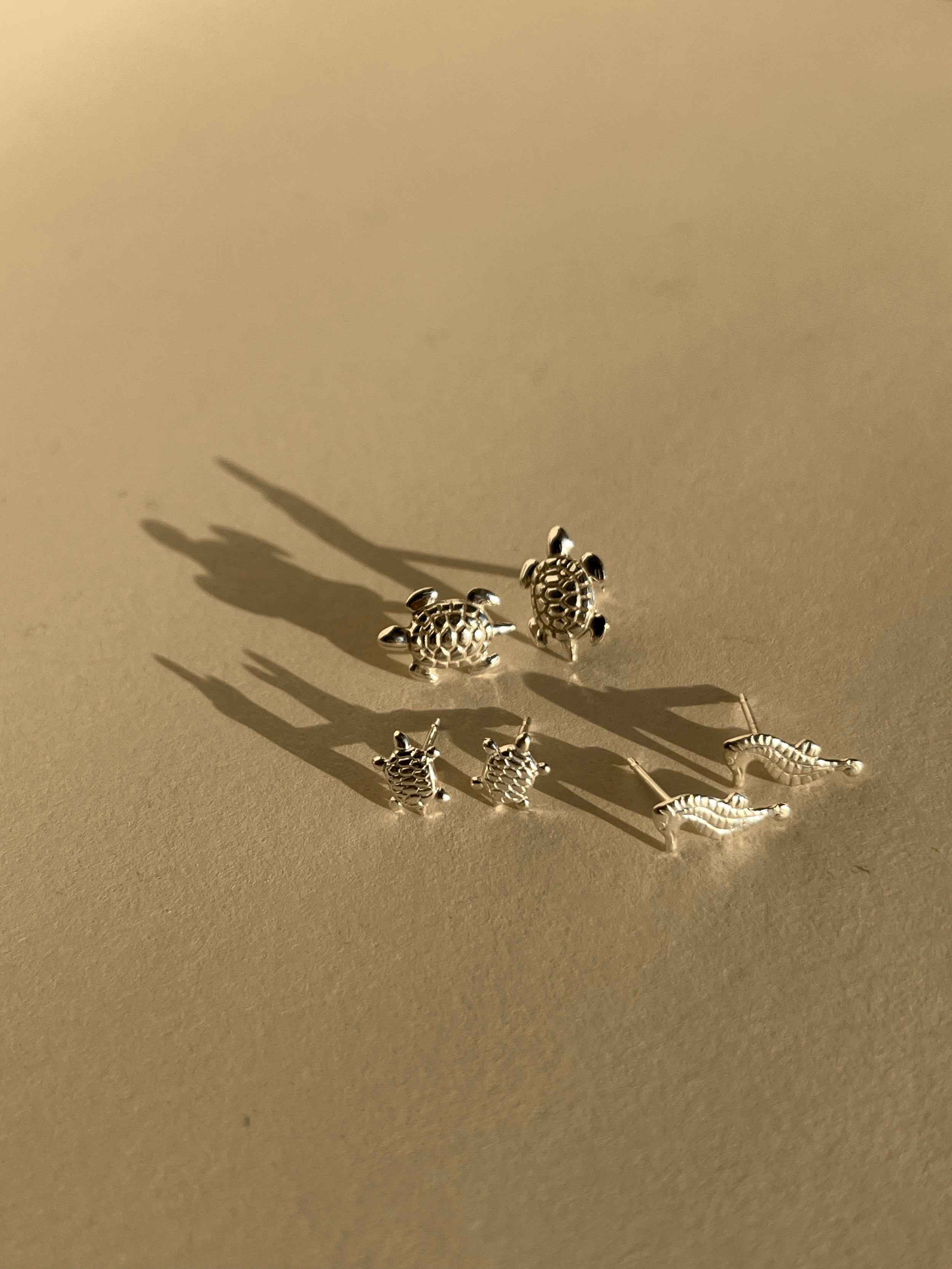 Pairs of large turtle, small turtle, and seahorse sterling silver stud earrings displayed on a neutral background