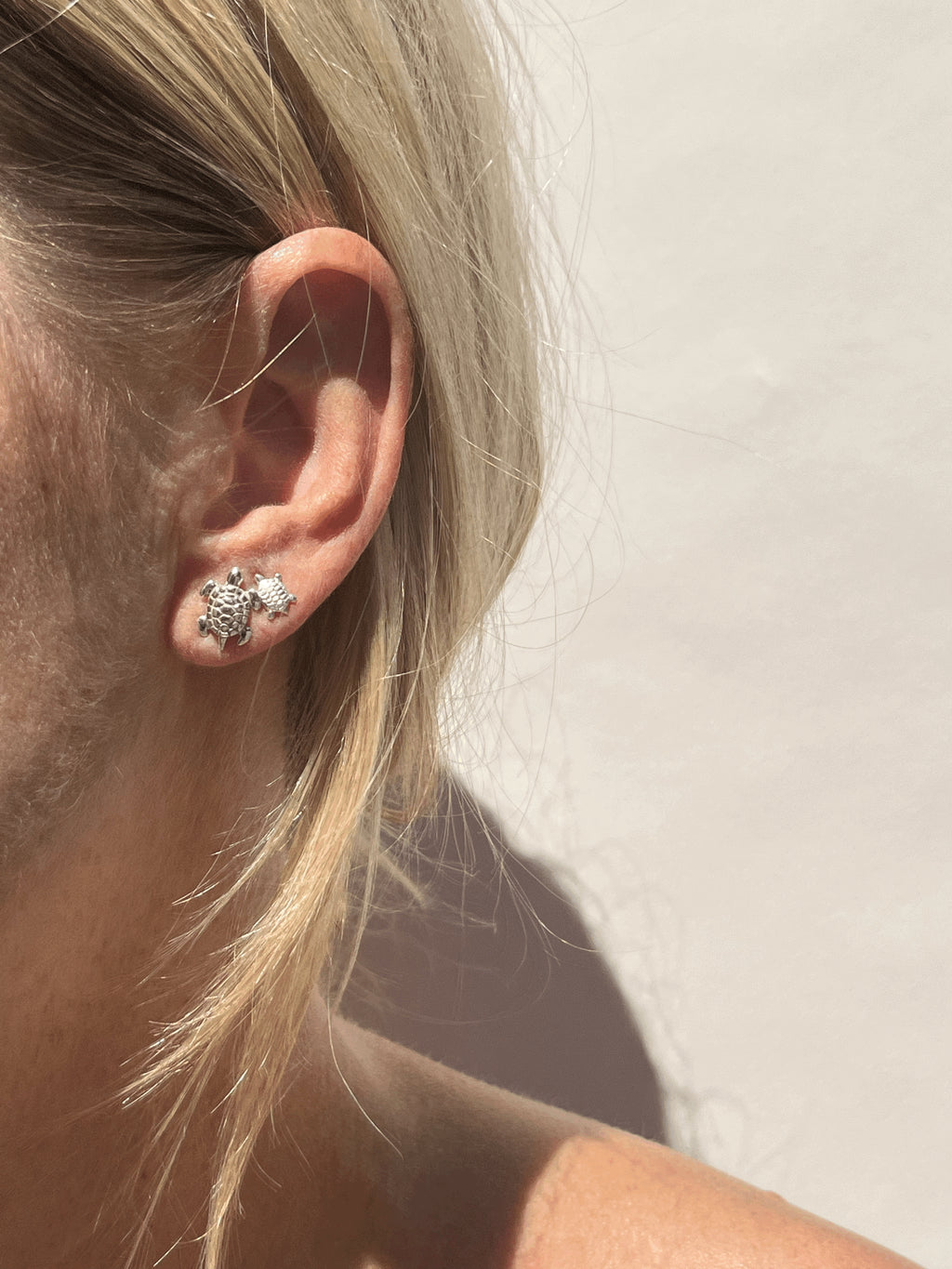 Model wearing a large sterling silver turtle stud in her first ear piercing and a small sterling silver turtle stud in her second ear piercing