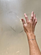 Hand model wearing the Water Baby light-blue cord bracelet with natural aquamarine, drawing a heart on a steamy shower door