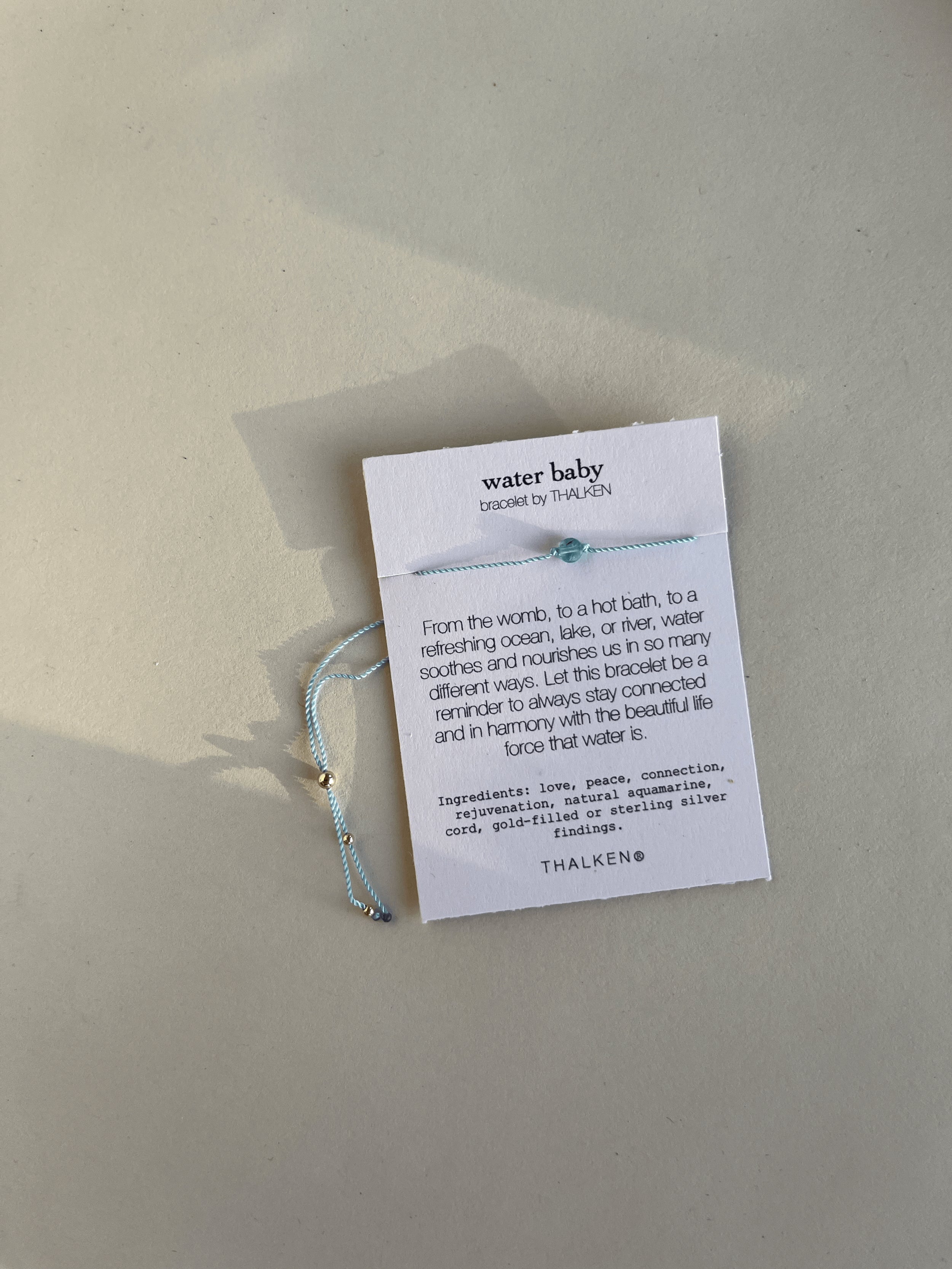 Close-up of Water Baby light-blue cord bracelet with natural aquamarine on its printed bracelet card