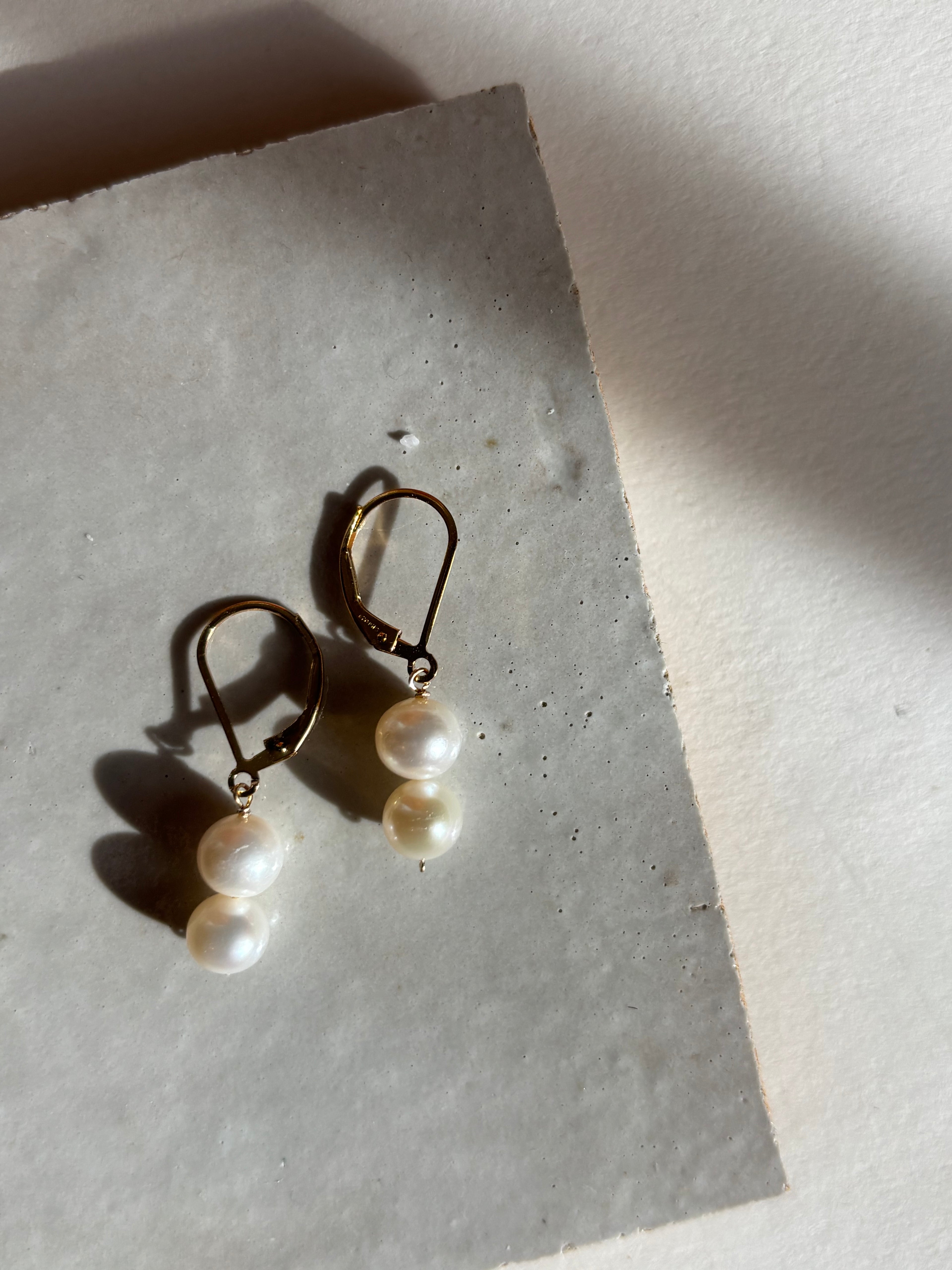 Close-up of the white double pearl drop detail on leverback earrings with warm, moody lighting.