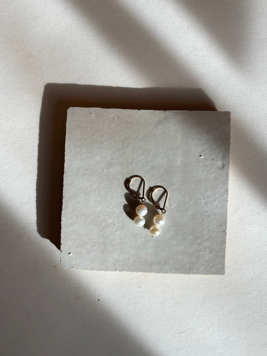 White double pearl drop on leverback earrings with warm, moody lighting.