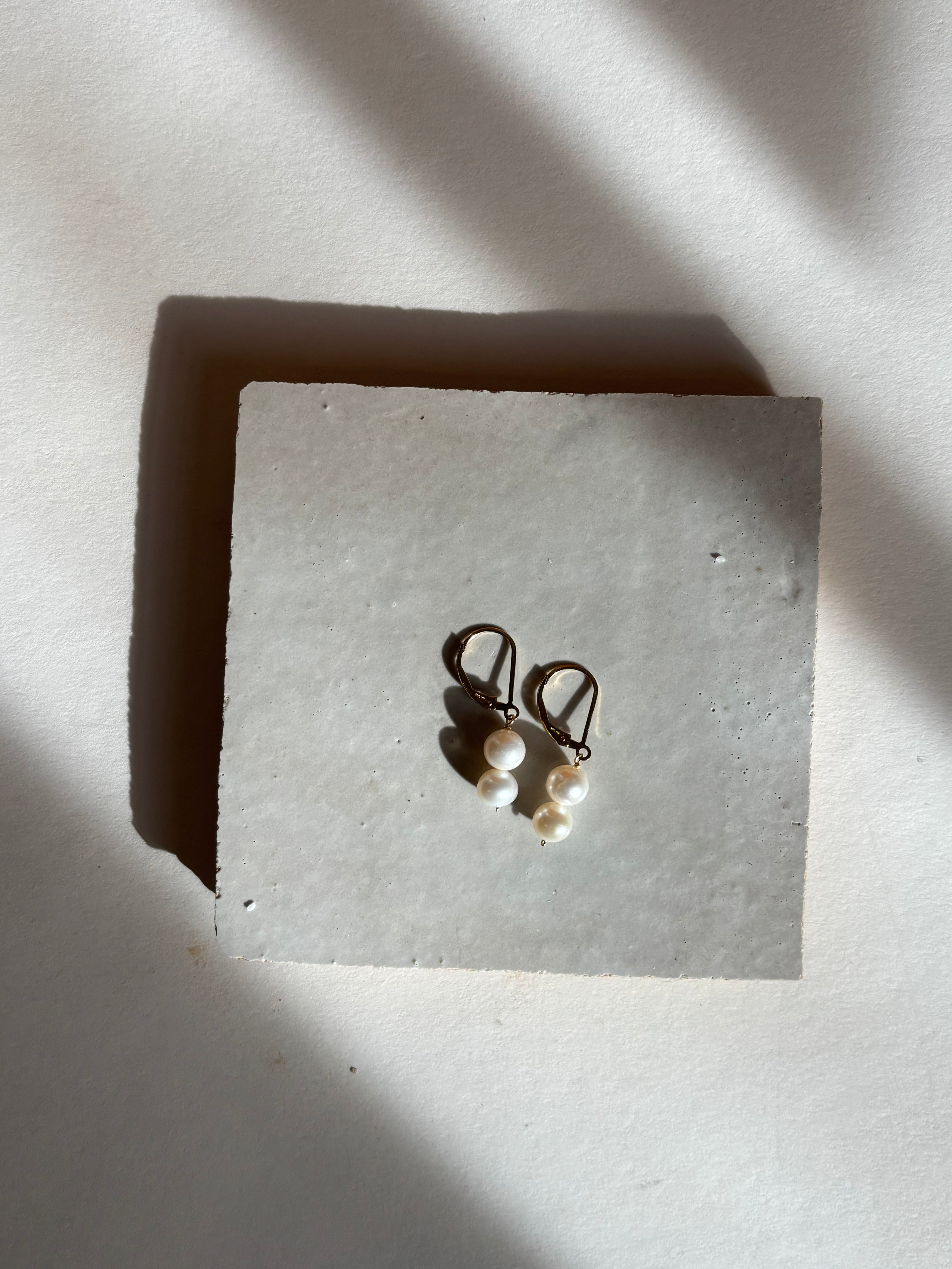 White double pearl drop on leverback earrings with warm, moody lighting.