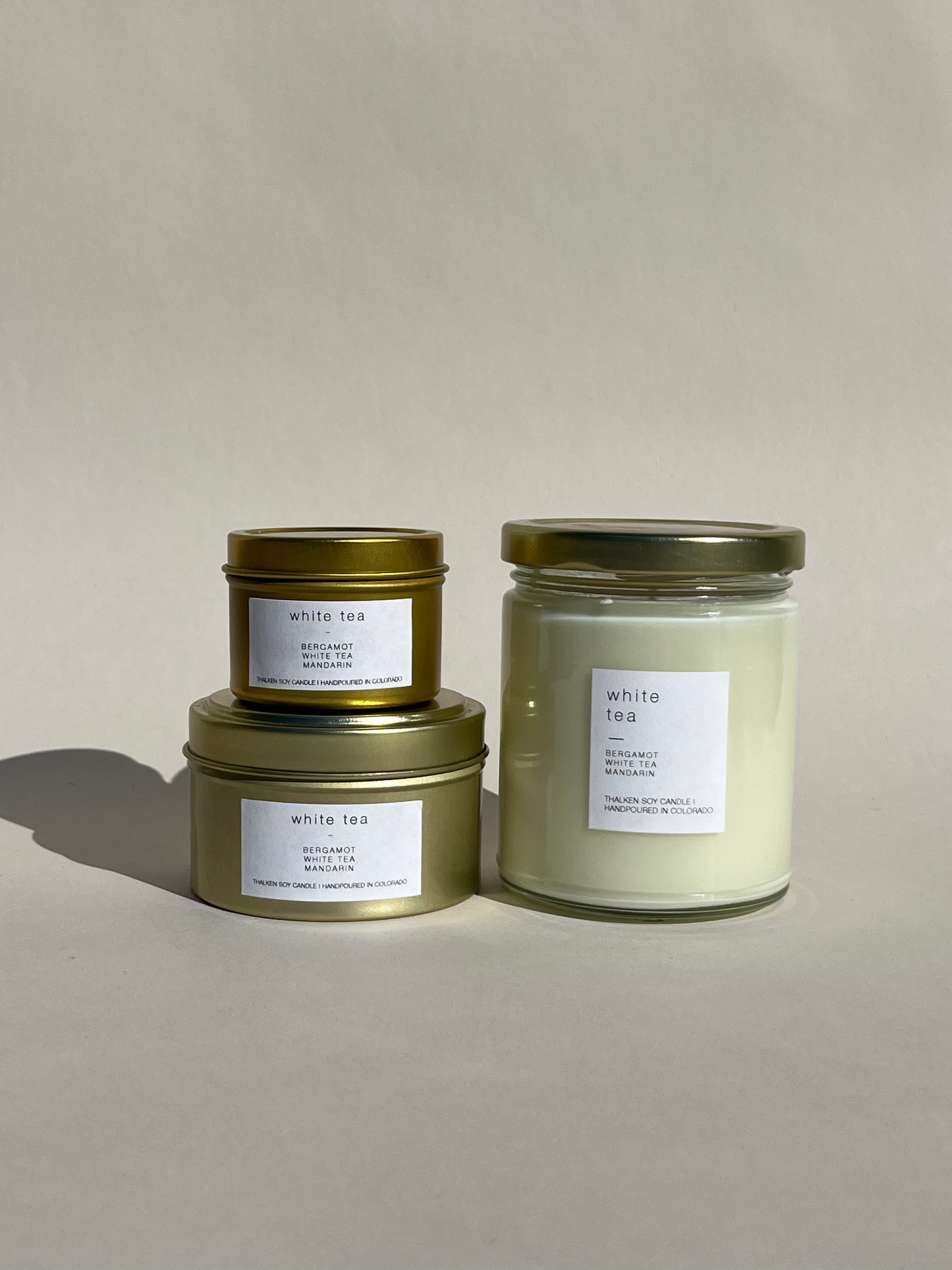 Thalken® White Tea candles in three sizes — 2oz and 6oz gold tins and 8oz soft-glow glass jar. Scent profile: airy and ethereal with bergamot, white tea buds, and mandarin