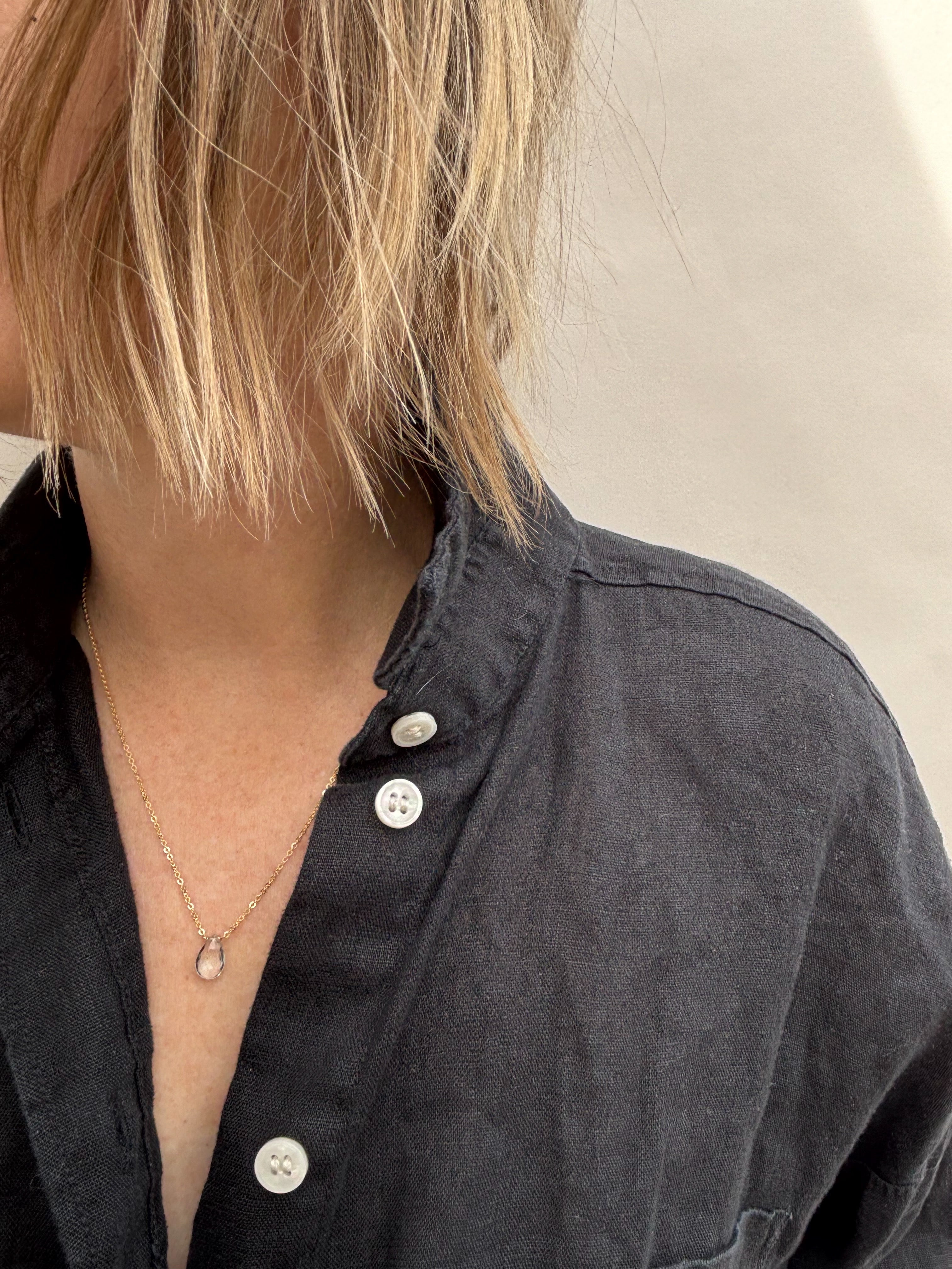 Minimalist white topaz necklace on woman looking away from the camera wearing black linen button down shirt with white buttons