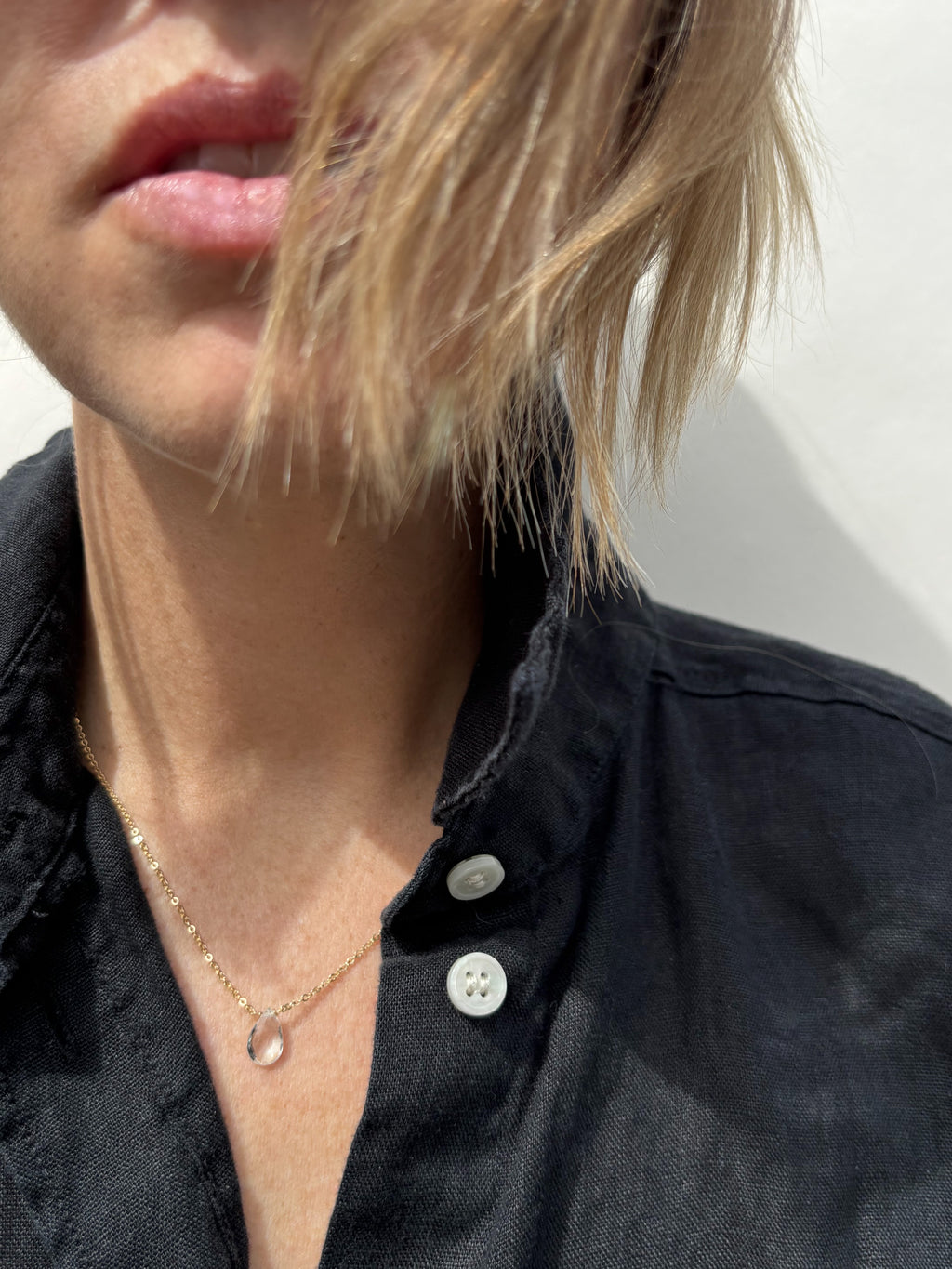 Minimalist white topaz necklace on woman wearing black linen button down shirt with white buttons