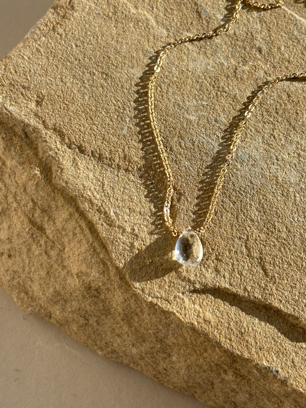 Thalken Natural White Topaz Drop Necklace draped over a rock in warm natural light close-up