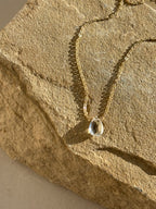 Thalken Natural White Topaz Drop Necklace draped over a rock in warm natural light close-up