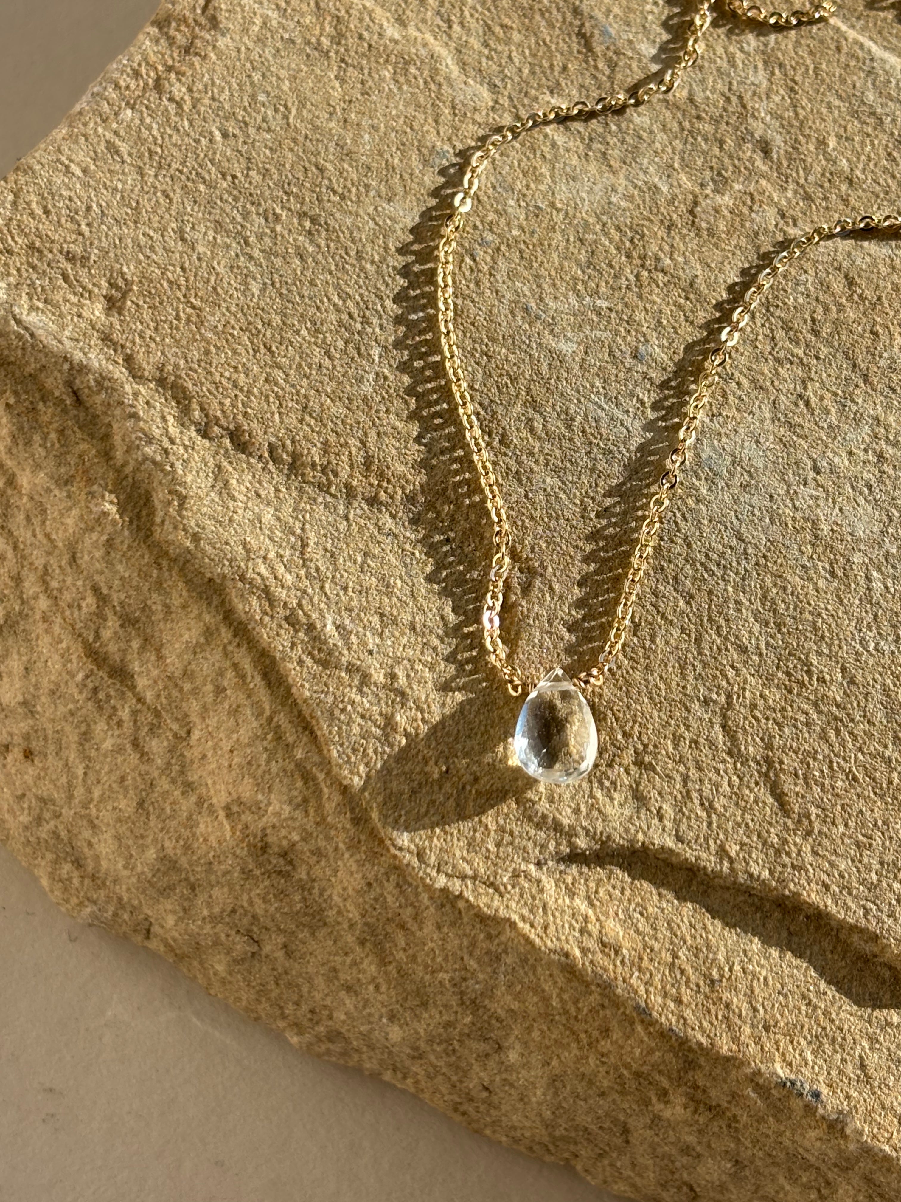 Thalken Natural White Topaz Drop Necklace draped over a rock in warm natural light close-up