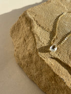 Thalken Natural White Topaz Drop Necklace draped over a rock in warm natural light