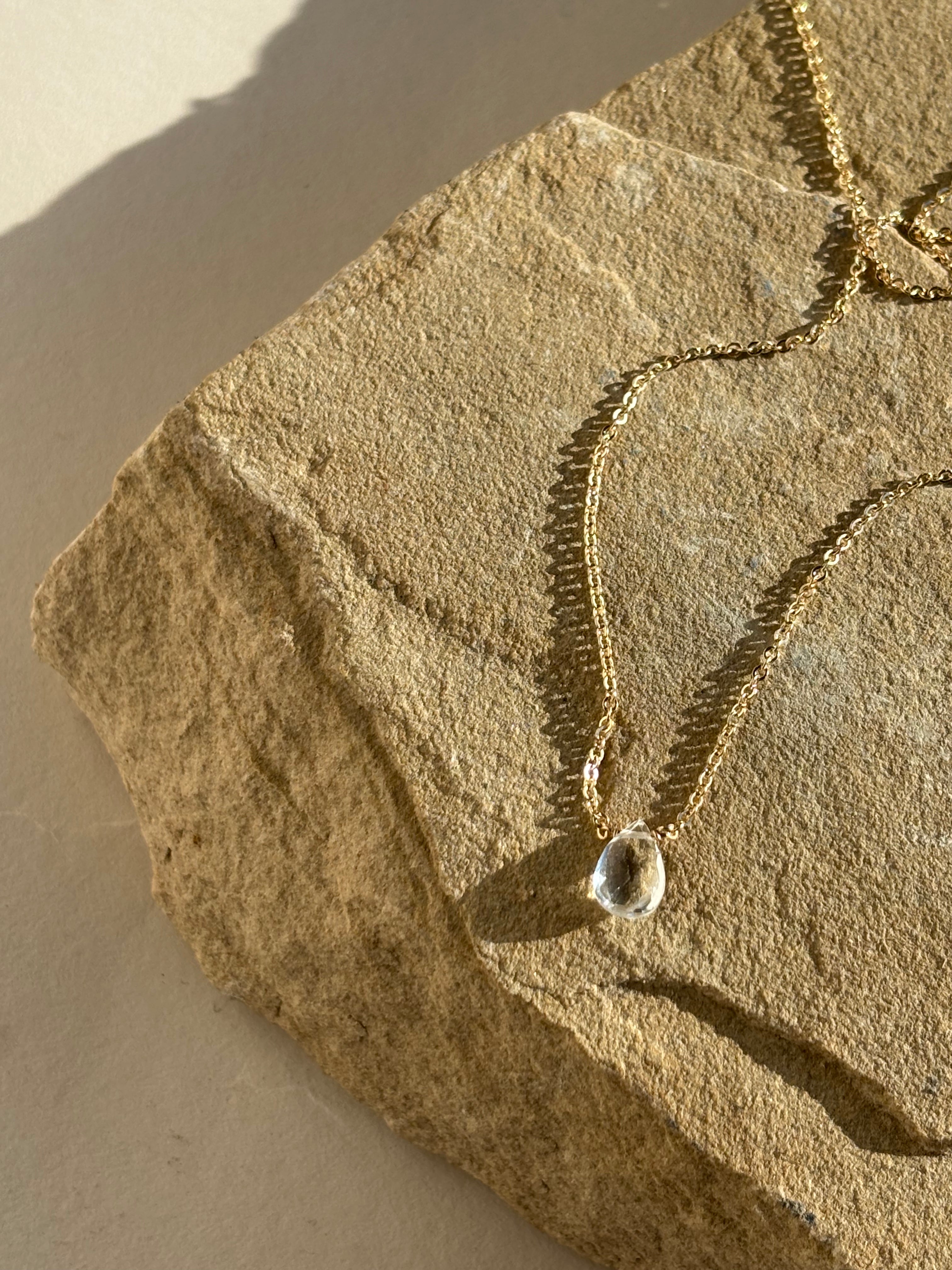 Thalken Natural White Topaz Drop Necklace draped over a rock in warm natural light