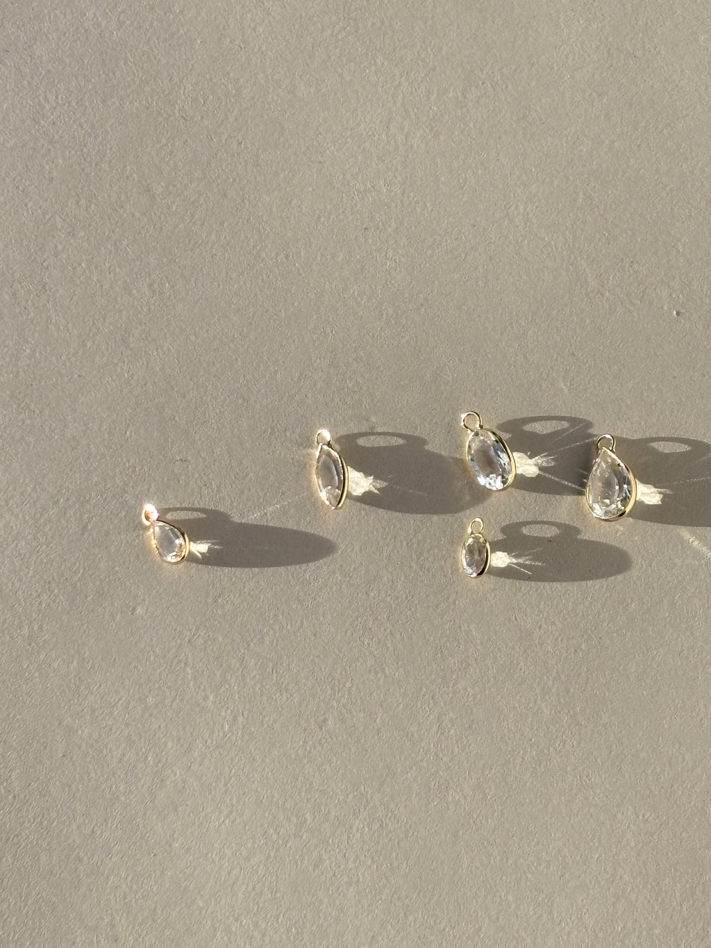 Assortment of Thalken 14k gold single drop earring charms in white topaz, displayed in pear, oval, and marquise shapes, unattached to hoops for customizable styling