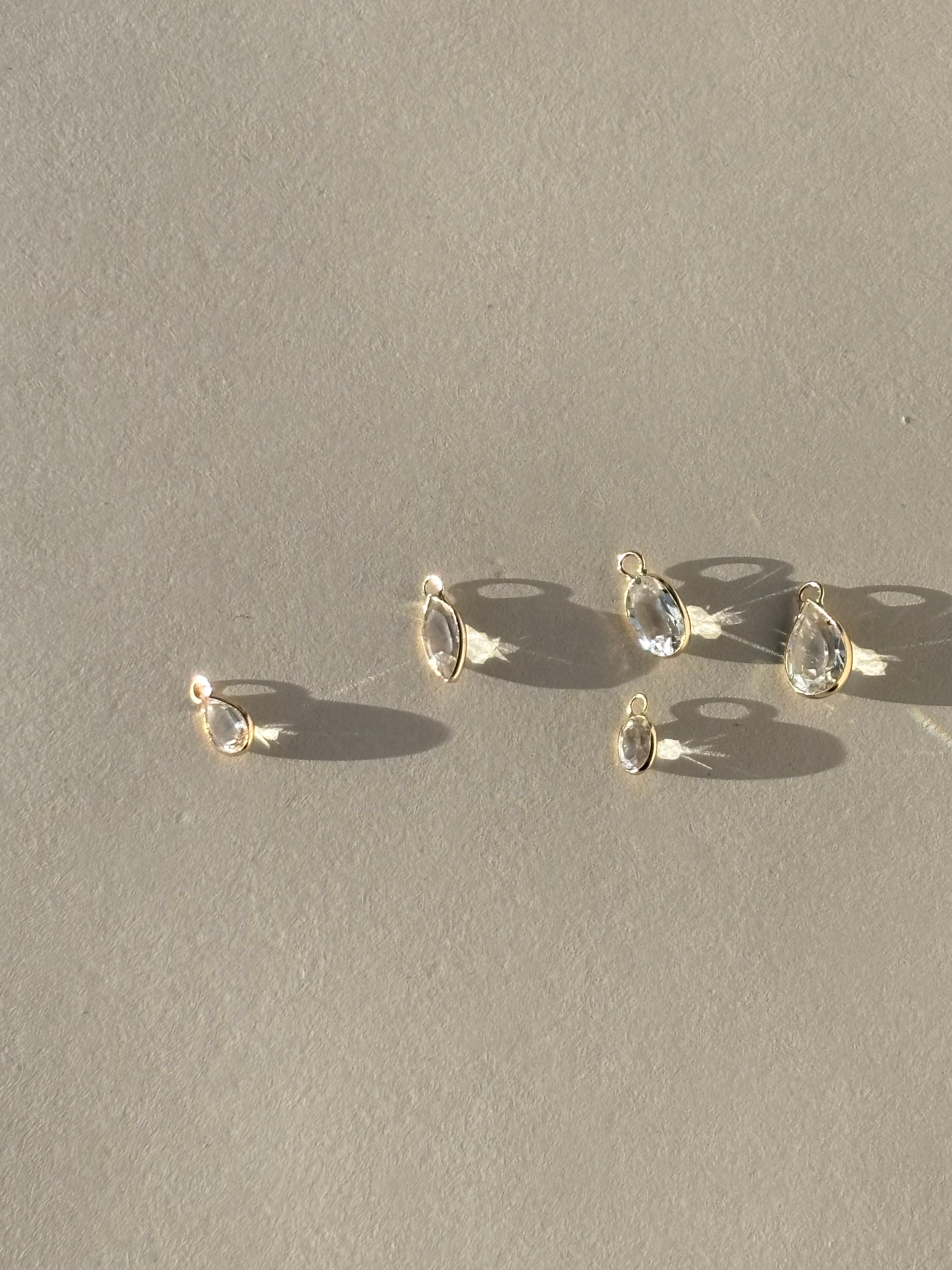 Assortment of Thalken 14k gold single drop earring charms in white topaz, displayed in pear, oval, and marquise shapes, unattached to hoops for customizable styling