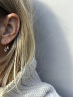 Model wearing Thalken 14k gold 12mm hoop earring with a large pear-shaped white topaz drop in the first ear piercing and a 10mm hoop with a small pear-shaped white topaz drop in the second ear piercing