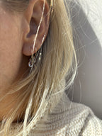 Model wearing Thalken 14k gold 12mm hoop earring with a large pear-shaped white topaz drop in the first ear piercing and a 10mm hoop with a small pear-shaped white topaz drop in the second ear piercing